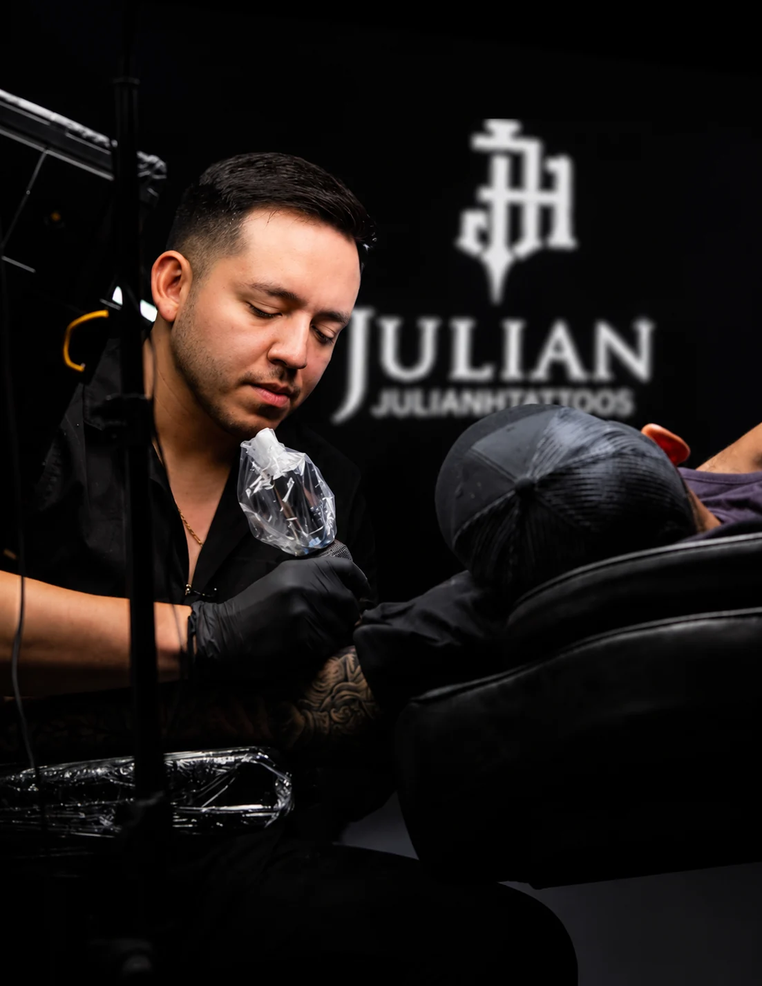 Julian tattooing with his studio logo behind him